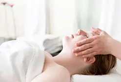 Kvinde får en anti-stress behandling af en terapeut, som holder sine hænder let på kvindens kinder
