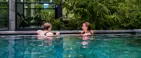 To kvinder i et udendørs bassin med grønt omkring