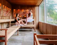 To kvinder i en sauna med himalaya-saltsten på væggen og grønt udenfor vinduet
