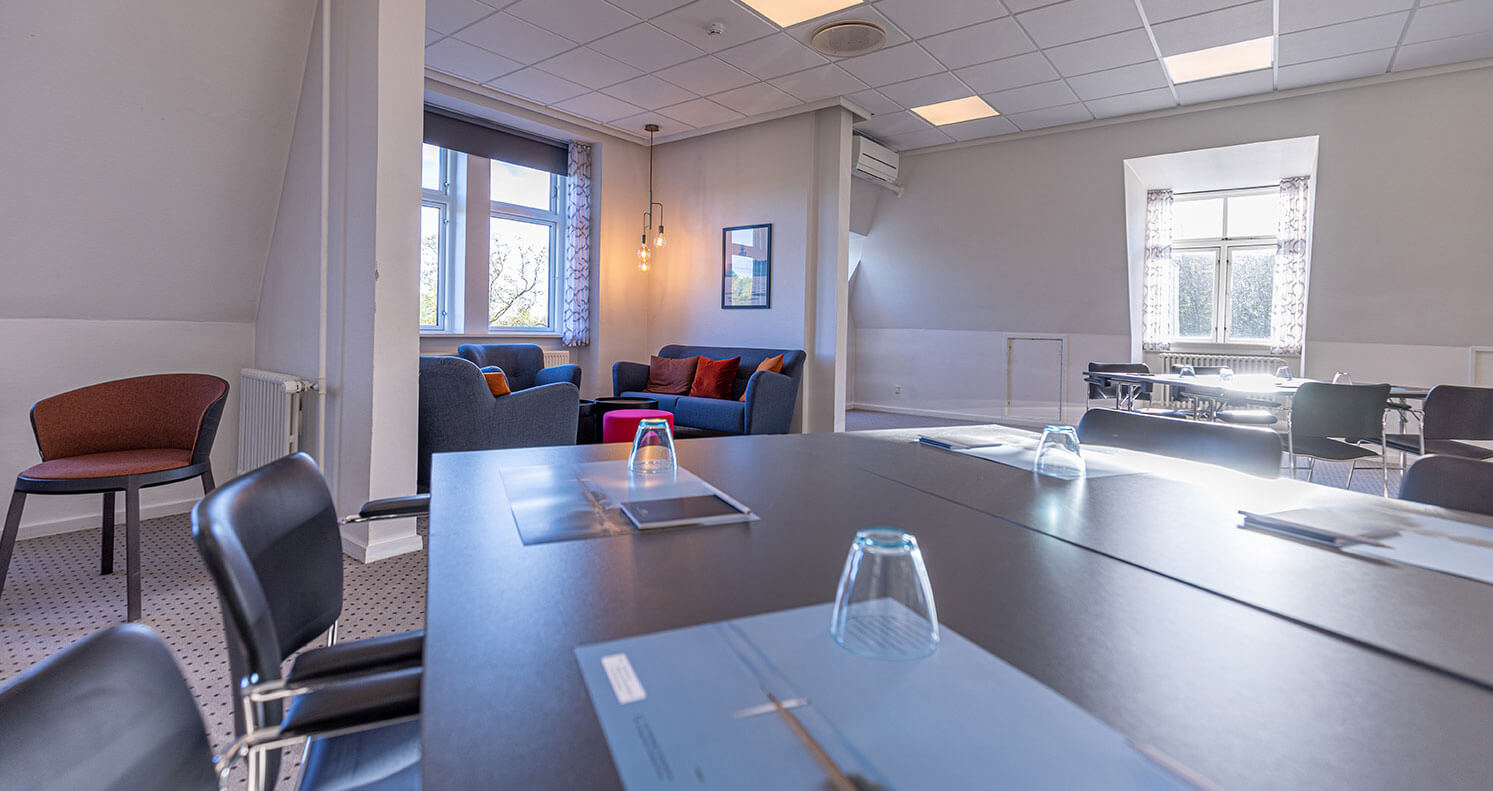 Mødelokale opstillet med gruppeborde og loungeområde i baggrunden