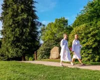 Kvinder i badekåber går på en sti i en park med en mindesten for Vejlefjords grundlæggelse
