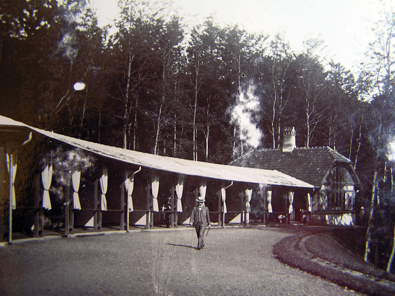 Et gammelt foto af en liggehal og en spadserende mand med hat