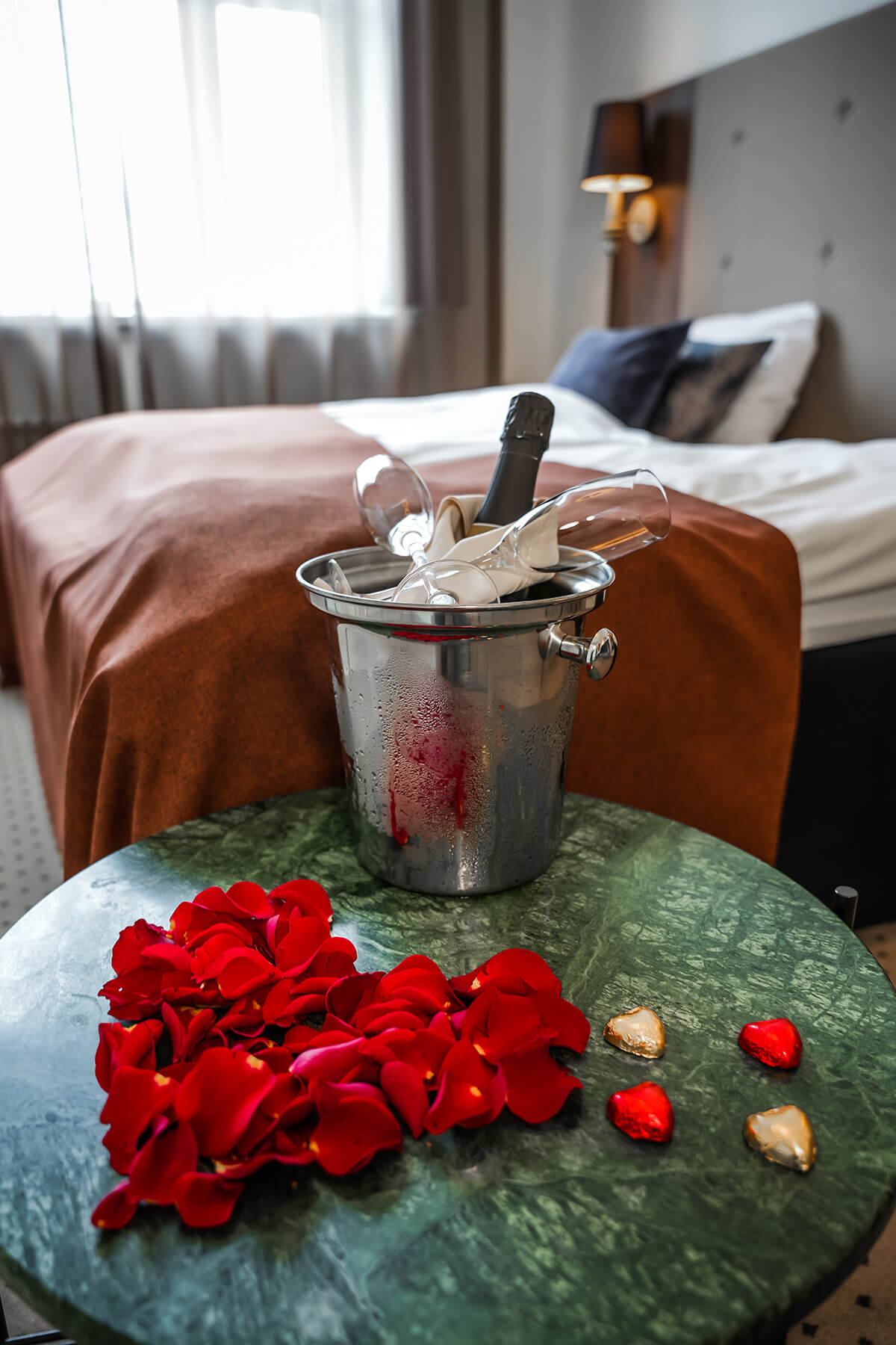 Et hotelværelse hvor der foran sengen står et bord med vinkøler og rosenblade