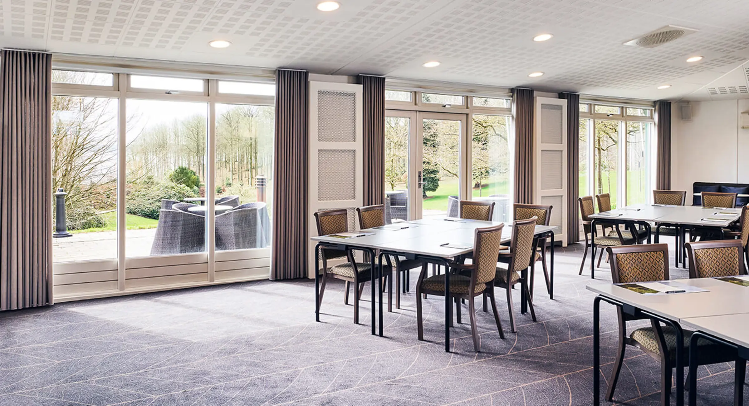 Mødelokale opstillet med gruppeborde og udsigt til park og terrasse