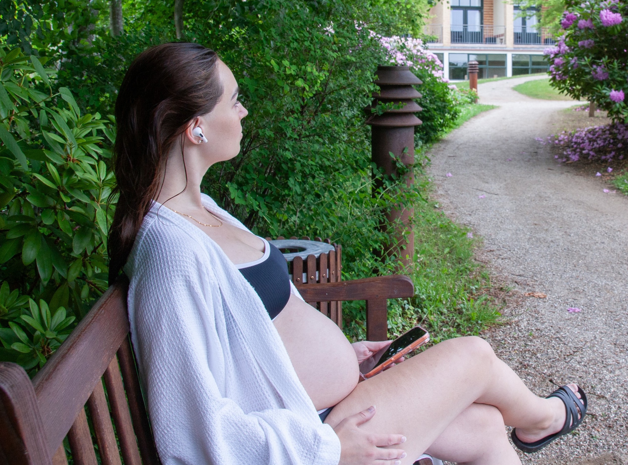 Gravid kvinde siddende på bænk med telefon og høretelefoner