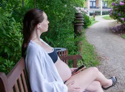 Gravid kvinde siddende på bænk med telefon og høretelefoner