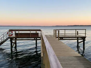 Hotel Vejlefjords badebro og fjordens blide bølger med blå/lyserød himmel