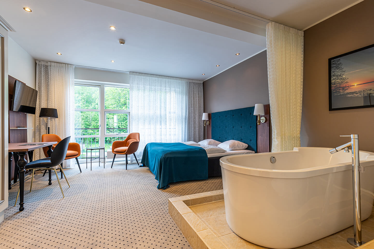 En juniorsuite med badekar og grøn skov udenfor vinduet