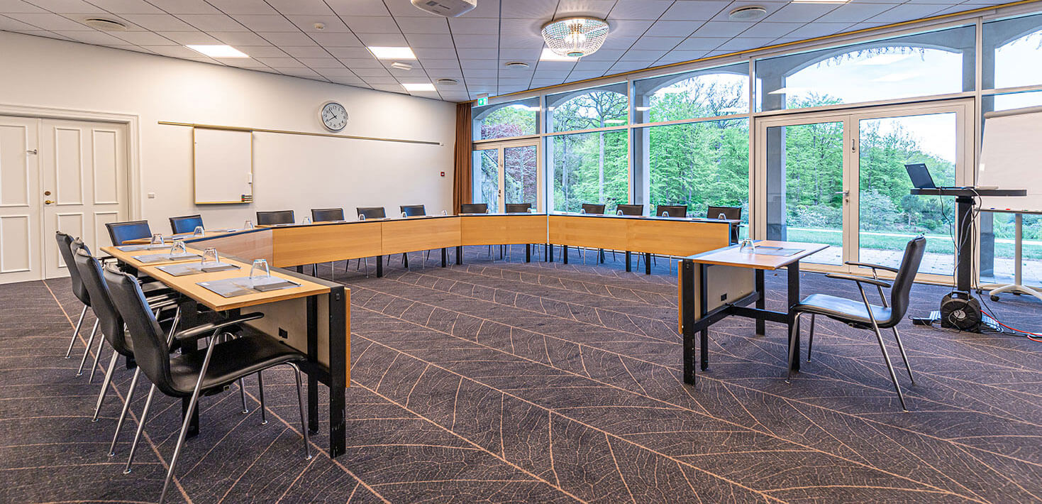 Konferencelokale med borde opstillet i hesteskoform - grøn natur udenfor vinduerne
