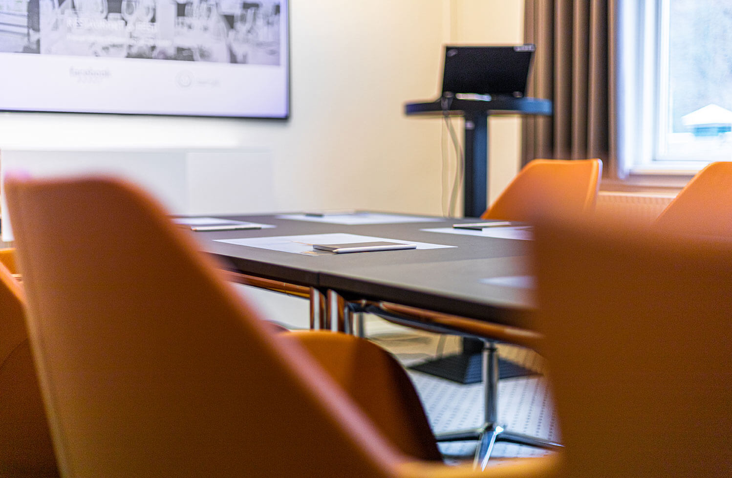 Cognacfarvede læderstole omkring et bord, i baggrunden er der en computer og en stor skærm 