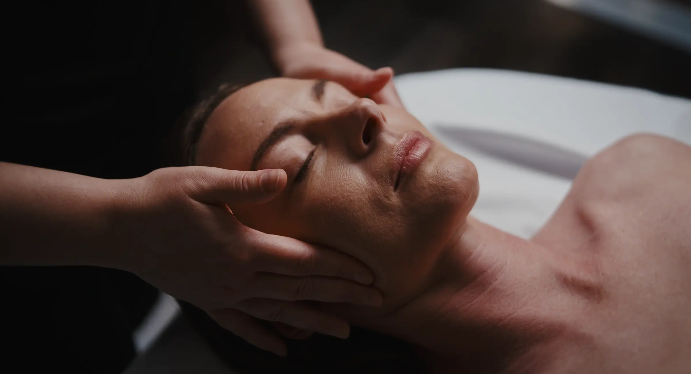 En kvinde er ved at få massage i et hyggeligt rum med levende lys