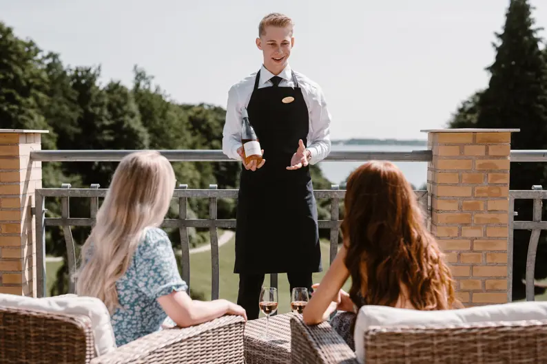 Et bord i en restaurant dækket op til middag, hvor to stole kigger ud på en parks flotte udsigt