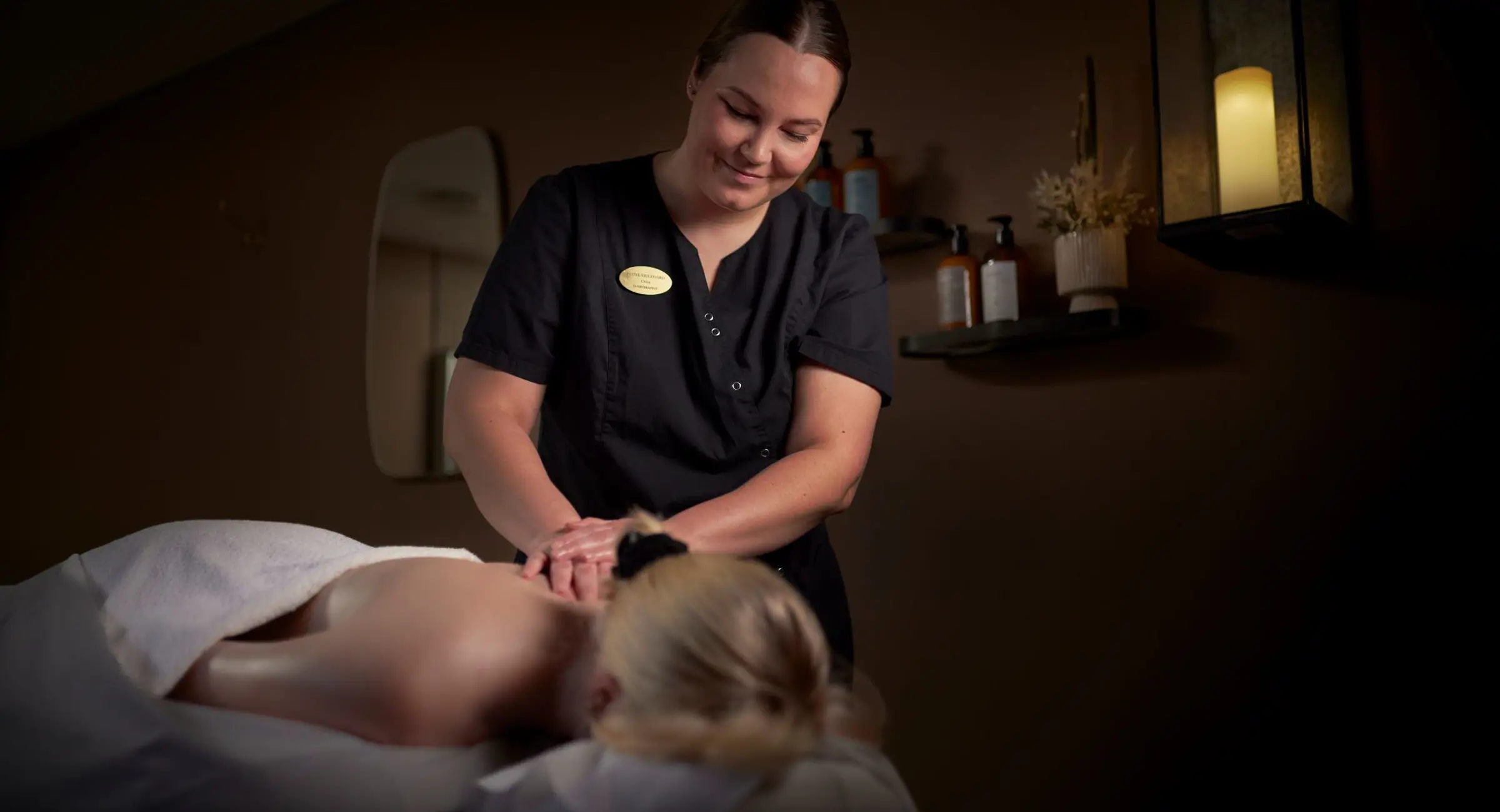 En massageterapeut er ved at give en kvinde massage i et hyggeligt mørkt rum med stearinlys