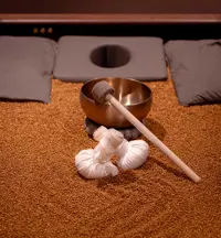 En del af en massagebriks med orange sand, klangskål og puder til hovedet