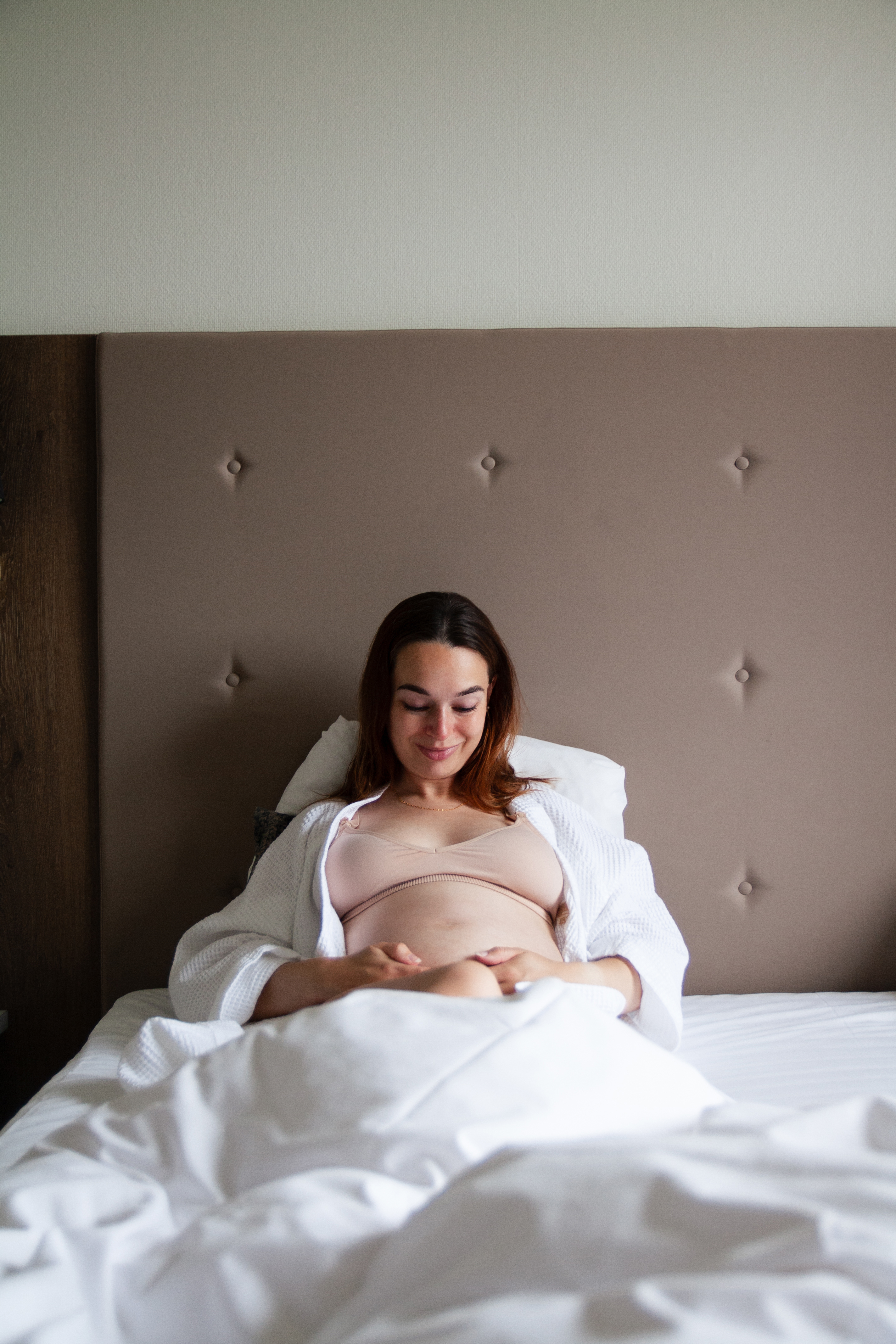 Gravid kvinde der sidder i sengen og nyder