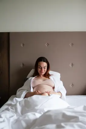 Gravid kvinde der sidder i sengen og nyder