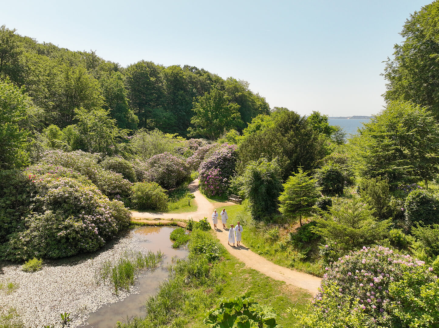 Dronefoto af stier i en grøn park, hvorpå der går spagæster i badekåber