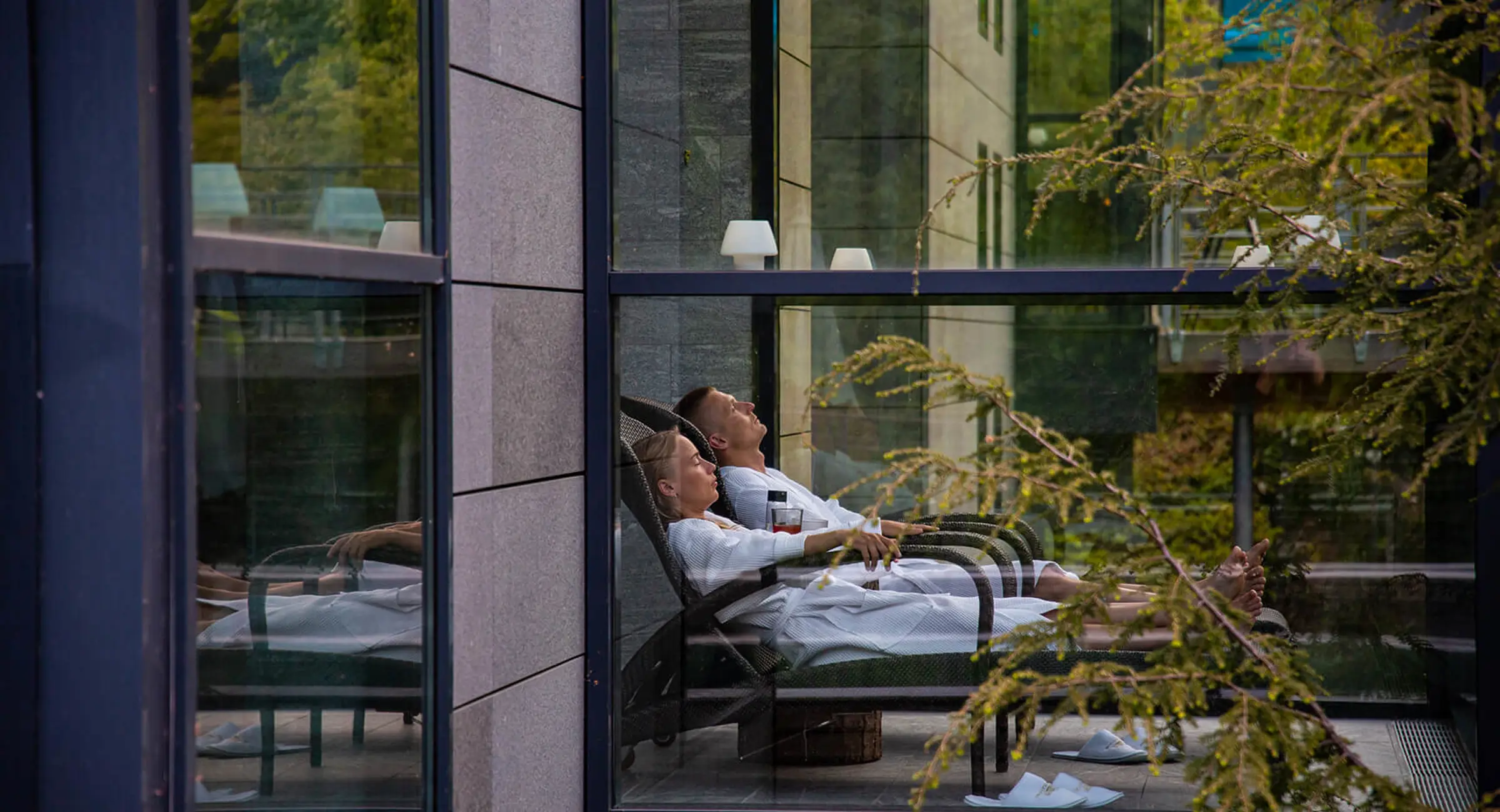 Et par i badkåber slapper af i liggestole i en spa omgivet af natur