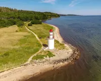 Et hvidt fyrtårn med rød top som ligger på en lille odde ved Vejle Fjord