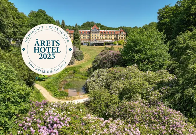 Hotellet set fra parken og blomstrende rhododendroner + Nominering som Årets Hotel 2025