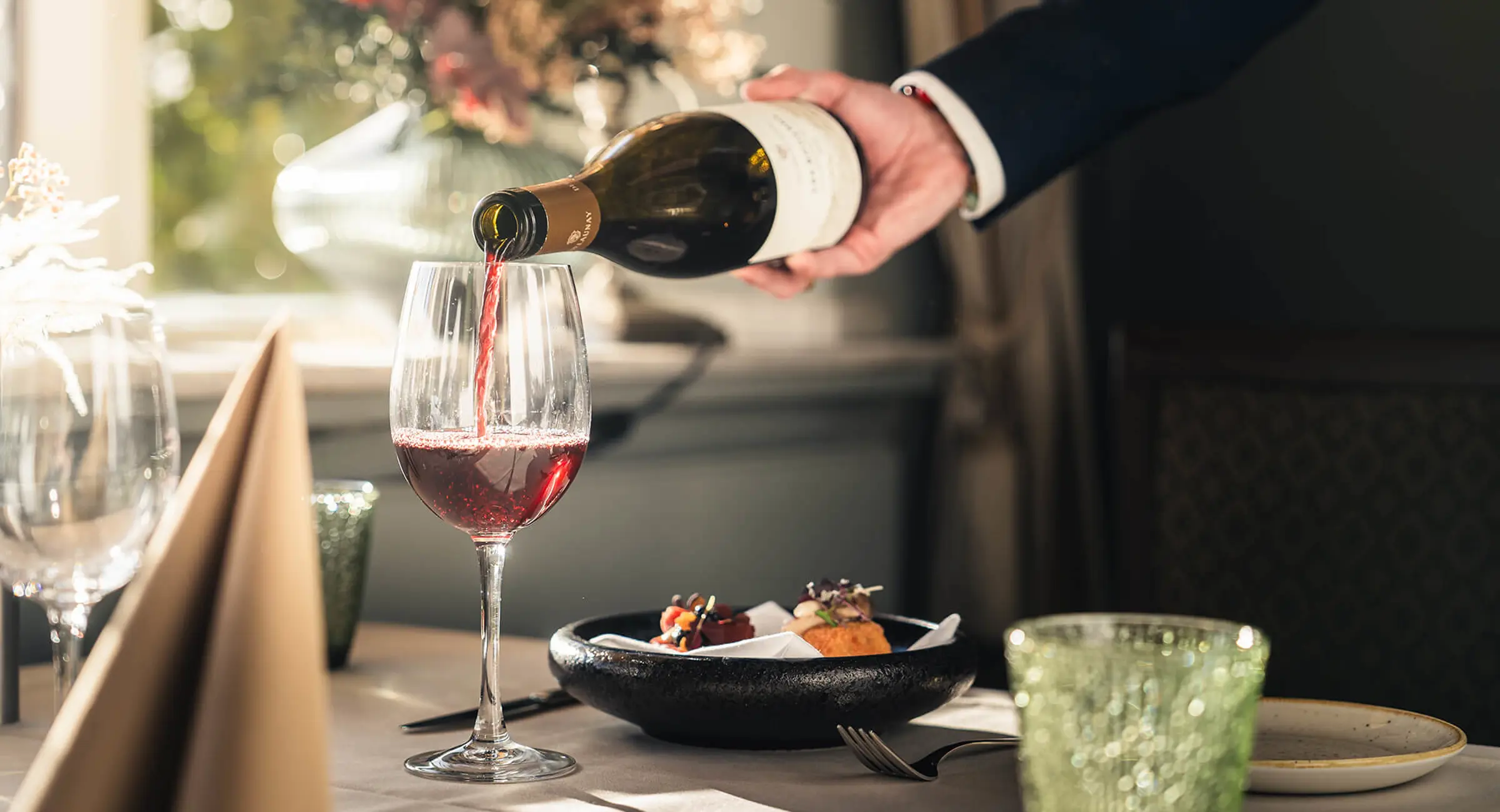 Tjener der hælder vin i glas og en appetizer der venter på at blive spist