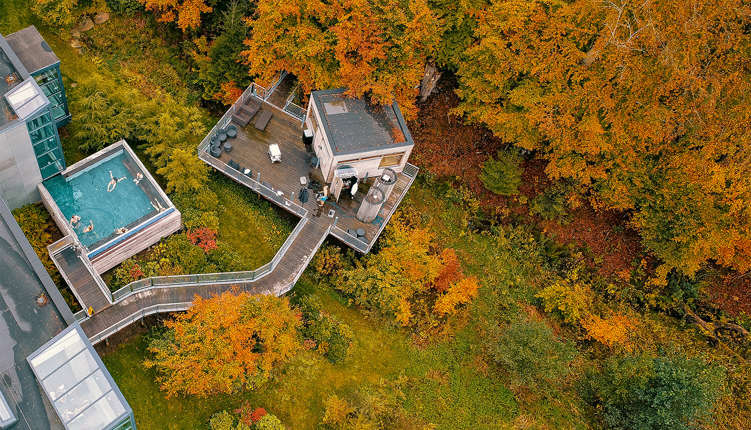 En udendørs spa med bassin og sauna omkranset af skov i efterårsfarver
